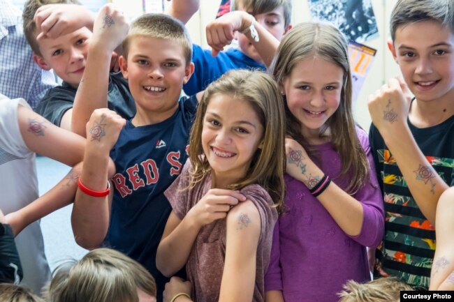 Students and their teacher show temporary tattoos they wear made from the drawing of a letter from Safiyo Noor Hassan, a student in Dadaab Refugee Camp. (Carey Wagner/CARE)