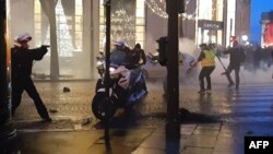 This frame from video taken Dec. 22, 2018, on the Champs-Elysees in Paris shows a police biker, left, drawing a weapon as he and other police are assaulted by protesters, during the sixth consecutive Saturday of mobilization of the "yellow vests."