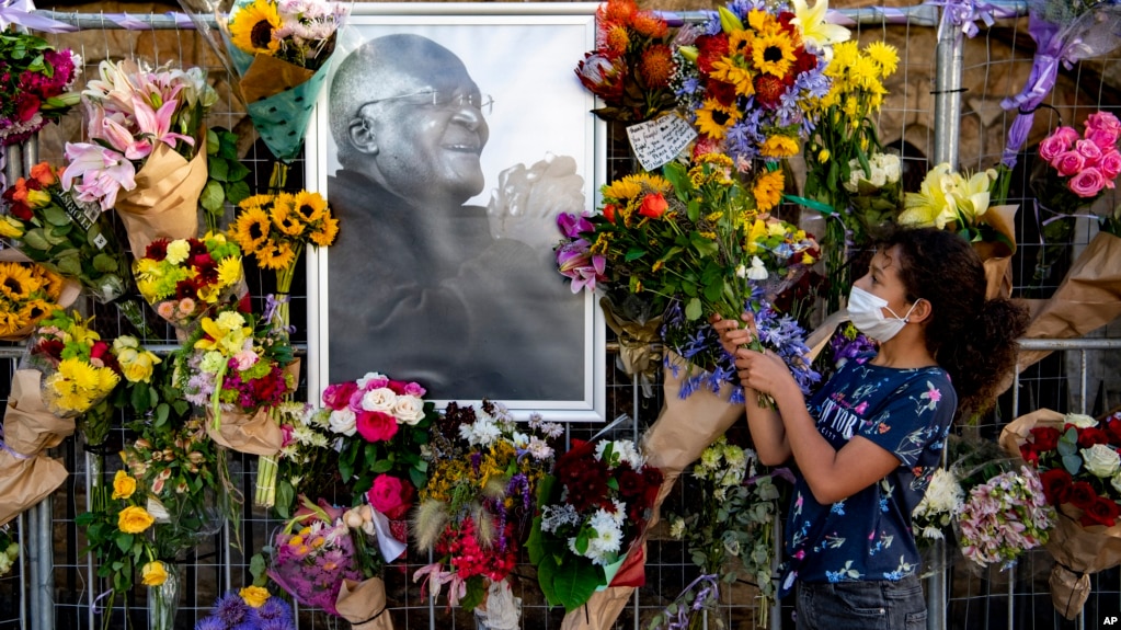 Flowers are placed on a fence surround a portrait of former Anglican Archbishop Desmond Tutu outside St. George's Cathedral in Cape Town, South Africa, Dec. 27, 2021. At midday bells are rung to honor Tutu, a day after his death. (AP Photo)