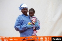 FILE - Victorine Siherya, an Ebola survivor working as a caregiver to babies who are confirmed Ebola cases, holds an infant outside the red zone at the Ebola treatment center in Butembo, Democratic Republic of Congo, March 25, 2019.