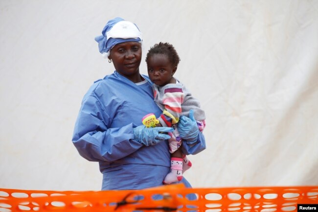 FILE - Victorine Siherya, an Ebola survivor working as a caregiver to babies who are confirmed Ebola cases, holds an infant outside the red zone at the Ebola treatment center in Butembo, Democratic Republic of Congo, March 25, 2019.