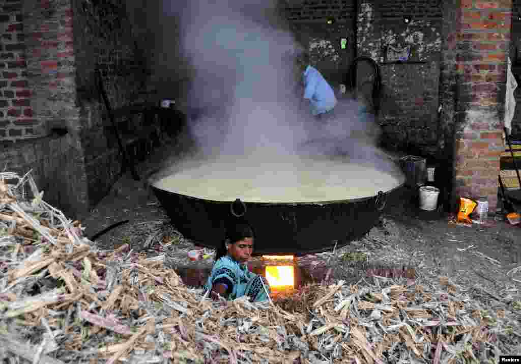 A woman gathers dried stalks of sugarcane to fuel a fire to prepare jaggery on the outskirts of Bengaluru, India,.