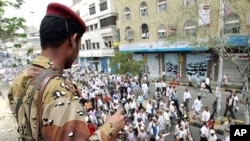 Army soldier watches as anti-government protesters march during a demonstration demanding the ouster of Yemen's President Ali Abdullah Saleh in the southern city of Taiz, April 26, 2011