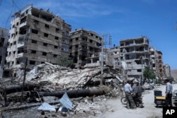在这张2018年4月16日拍摄的照片中，人们站在叙利亚大马士革附近杜马镇受损的建筑物前，这里是疑似化学武器袭击的地点。
