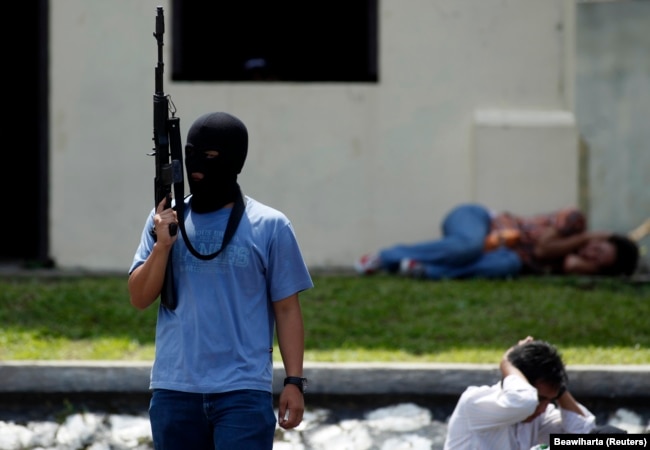 Seorang teroris tiruan memegang senapan di dekat "warga sipil yang ditahan" dalam latihan anti-teror di markas pasukan khusus polisi di Depok, Jawa Barat, 9 Maret 2010. (Foto: REUTERS/Beawiharta)