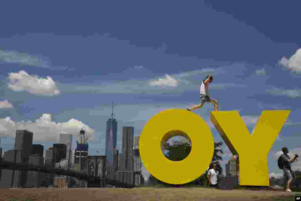 A visitor jumps between the letters of Deborah Kass' sculpture OY/YO, at the Brooklyn Bridge park in New York.