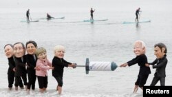 资料照片：慈善机构乐施会活动人士在英国康沃尔海滩上戴上七国集团领导人的漫画大头像假装在争夺新冠病毒疫苗。（2021年6月11日）