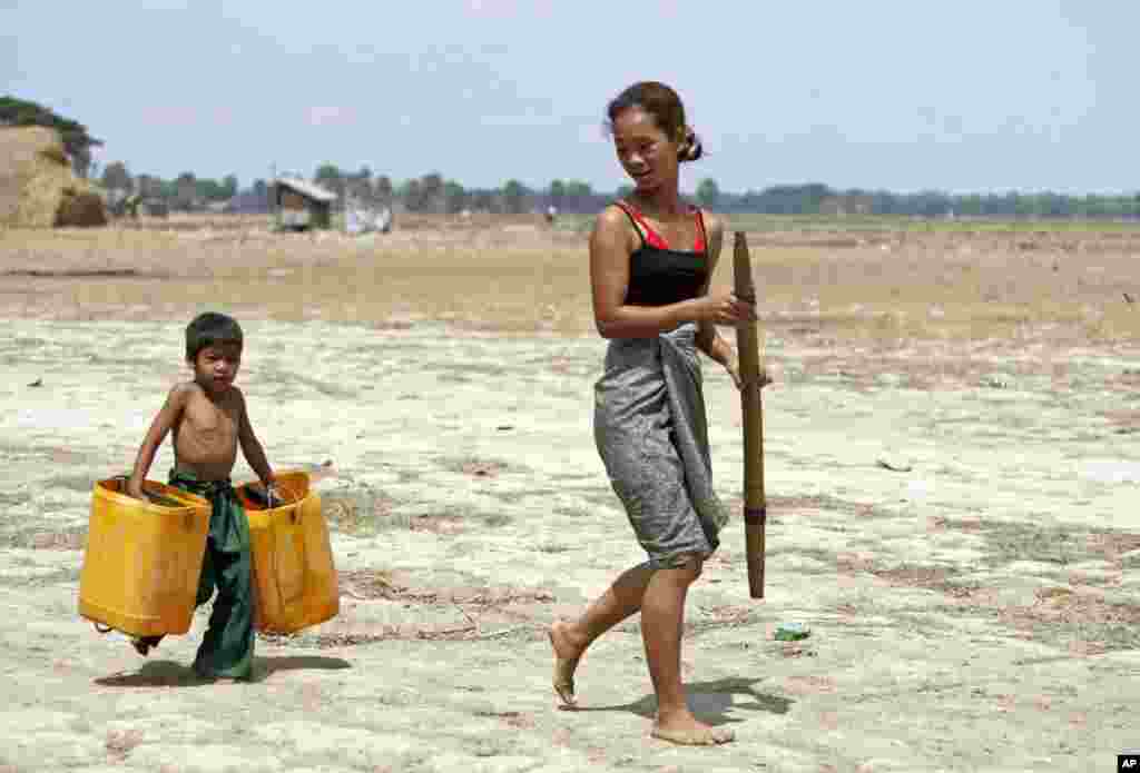A boy carrying empty plastic containers follows his mother to help her fetch water, in Dala township, about 15 kilometers (9 miles) south of Rangoon, Burma. Several regions and states face acute water shortage especially in the summer. 