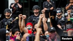 Seattle Police officers look on as people raise their fists while singing "Lift Every Voice and Sing" during a protest calling for a 50% defunding of the Seattle Police Department and investment in community based solutions in Seattle, Washington, U.S. Ju