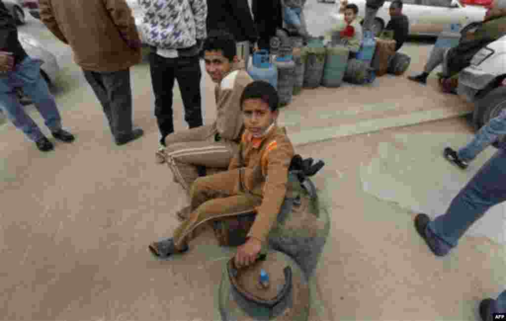 Two Libyan children wait by empty cooking gas cylinders as they queue in front of a cooking gas storage house in Benghazi, Libya Sunday, March 13, 2011. Libyans queued during the day in Benghazi for cooking gas in front of storage houses that suffer sever