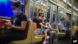 Archivo - En esta foto del 17 de agosto del 2020, una niña descansa en el regazo de su madre en un tren del metro de Nueva York, donde los pasajeros lucen mascarillas por la pandemia de coronavirus. (AP Foto/John Minchillo)