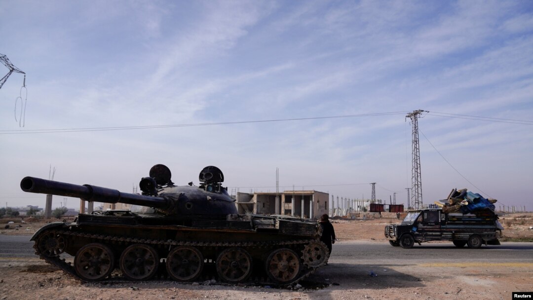 Sebuah mobil bergerak melewati tank yang terabaikan di Aleppo, Suriah, pada 11 Desember 2024. (Foto: Reuters/Karam al-Masri)