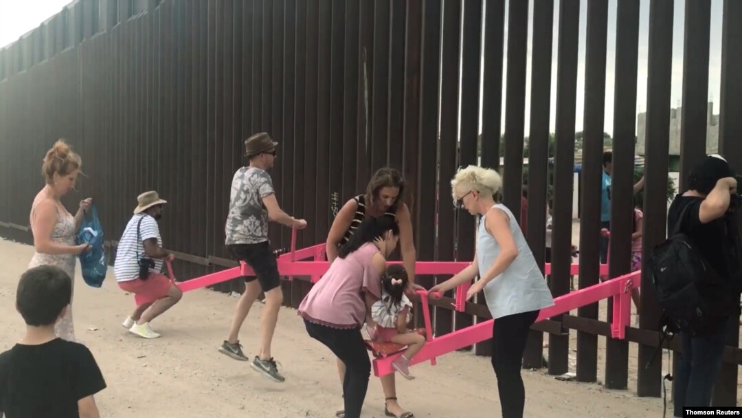 People play on a set of fluorescent pink seesaws across the U.S.-Mexico border in Sunland Park, NM, in this still image taken from social media video, July 28, 2019. 