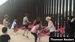 People play on a set of fluorescent pink seesaws across the U.S.-Mexico border in Sunland Park, NM, in this still image taken from social media video, July 28, 2019. 