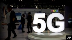 Visitantes se paran cerca de un logotipo 5G en una pantalla del fabricante chino de cables de fibra óptica YOFC en la PT Expo en Beijing. 