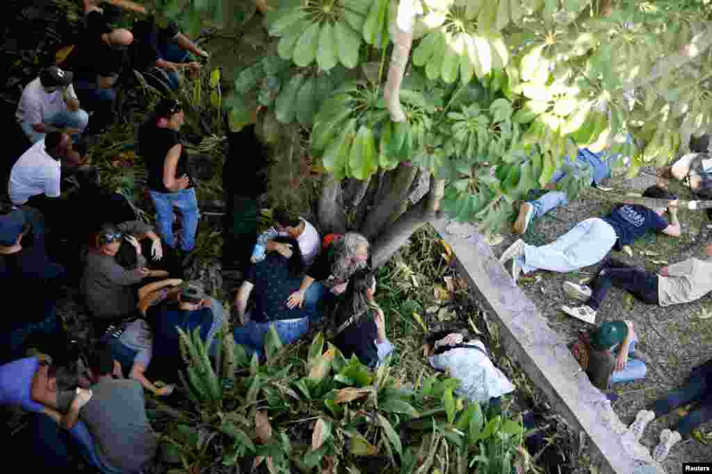 People lay and sit on the ground as sirens sound during the funeral of Sivan Sadeh, who was killed during a rocket attack from Lebanon, amid cross-border hostilities between Hezbollah and Israel, in Kibbutz Kfar Masaryk, northern Israel.