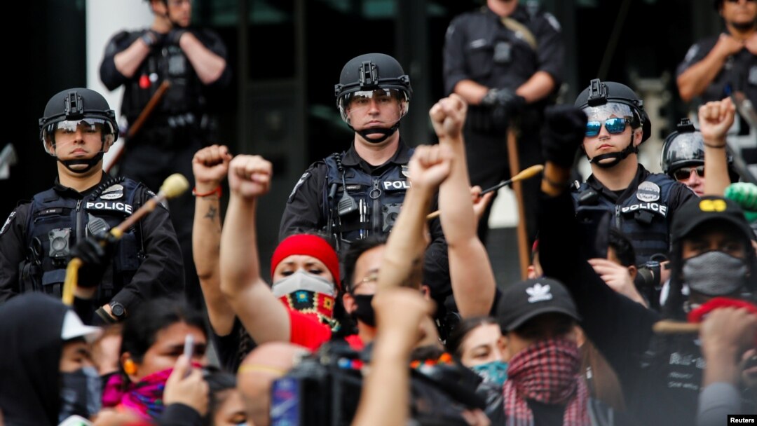 Seattle Police officers look on as people raise their fists while singing "Lift Every Voice and Sing" during a protest calling for a 50% defunding of the Seattle Police Department and investment in community based solutions in Seattle, Washington, U.S. Ju