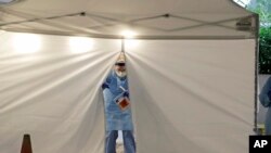 A nurse at a drive up COVID-19 coronavirus testing station set up by the University of Washington Medical Center exits a tent while holding a bag containing a swab used to take a sample from the nose of a person in their car, March 13, 2020, in Seattle.