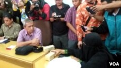 Suratmi (kanan, mengenakan baju warna hitam yang juga menutup wajahnya), istri terduga teroris Siyono yang tewas ketika diperiksa Densus 88 Selasa (29/3) menyerahkan 2 bungkusan uang kepada Busyro Muqodas Ketua PP Muhammadiyah Bidang hukum dan HAM. (VOA/