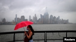A woman shields herself from rain and wind produced by Tropical Storm Fay with an umbrella as she walks along the Hudson River in front of the skyline of New York City, July 10, 2020.