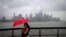 A woman shields herself from rain and wind produced by Tropical Storm Fay with an umbrella as she walks along the Hudson River in front of the skyline of New York City, July 10, 2020.