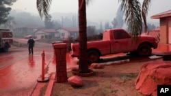 A truck and a street are covered in fire retardant dropped by an air tanker as crews battle a wildfire, Aug. 10, 2018, in Lake Elsinore, Calif. 