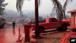 A truck and a street are covered in fire retardant dropped by an air tanker as crews battle a wildfire, Aug. 10, 2018, in Lake Elsinore, Calif. 