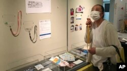 In this photo provided by curator Makoto Mochida of The Historical Museum of Urahoro, Shoko Maede, a nursery-school cook, looks at a display of masks at the museum, in Hokkaido, northern Japan on Aug. 14, 2020. (Makoto Mochida/The Historical Museum of Urahoro via AP)