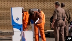 Un oficial observa cómo un recluso inserta su papeleta en la urna en el colegio electoral del Centro Correccional de Kgoši Mampuru en Pretoria, Sudáfrica, el miércoles 29 de mayo de 2024. 