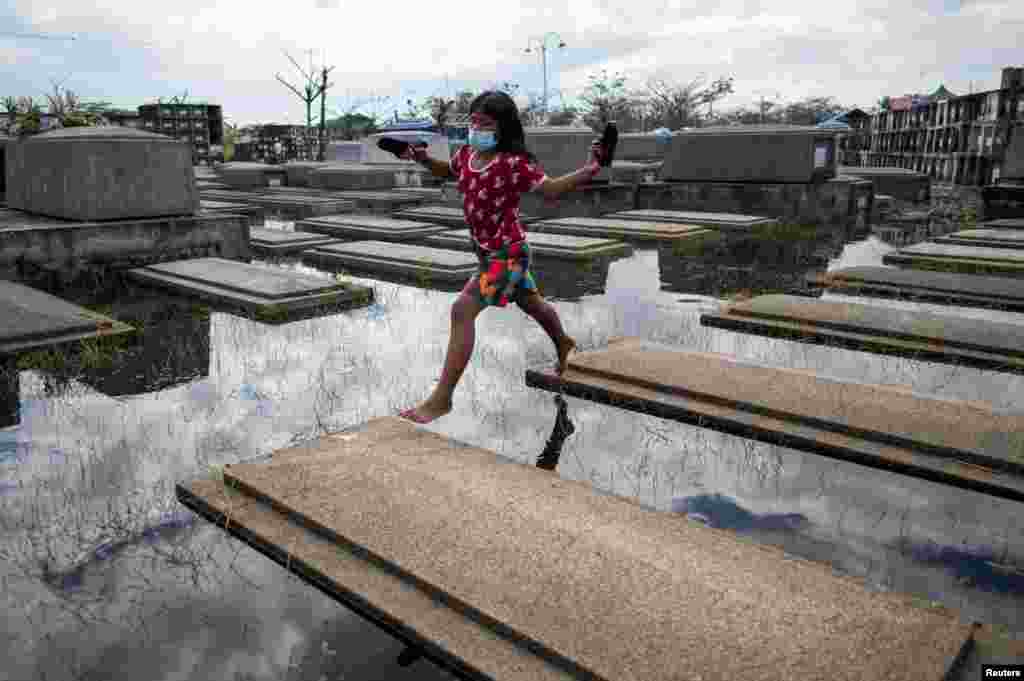 A girl jumps from a tomb, a day before the nationwide cemetery closure during All Saints&#39; Day at a flooded cemetery in Masantol, Pampanga, Philippines.