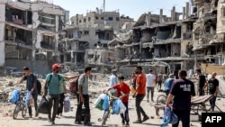 People walk past rubble and damaged buildings in the Tuffah district east of Gaza City on July 8, 2024 amid the ongoing conflict in the Palestinian territory between Israel and Hamas.