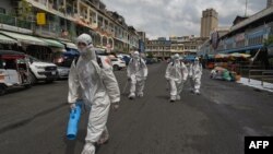 Workers wearing personal protective equipment (PPE) carry disinfectant to be sprayed at the Orussey market, after it was temporarily closed following a few vendors testing positive for the Covid-19 coronavirus, in Phnom Penh on April 4, 2021. (Photo by TANG CHHIN Sothy / AFP)