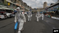 Workers wearing personal protective equipment (PPE) carry disinfectant to be sprayed at the Orussey market, after it was temporarily closed following a few vendors testing positive for the Covid-19 coronavirus, in Phnom Penh on April 4, 2021. (Photo by TANG CHHIN Sothy / AFP)