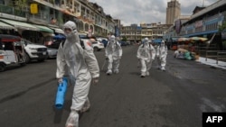 FILE - Workers wearing personal protective equipment (PPE) carry disinfectant to be sprayed at the Orussey market, after it was temporarily closed following a few vendors testing positive for the Covid-19 coronavirus, in Phnom Penh on April 4, 2021. (AFP)