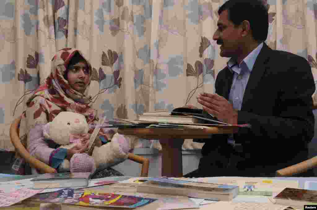 ໃນຮູບທີ່ນໍາອອກເຜີຍແຜ່ໃນວັນທີ 8 ພະຈິກ, 2012, ສາວນ້ອຍນັກຮຽນປາກິສຖານ Malala Yousufzai ລົມນໍາພໍ່ຂອງນນາງ, ທ່ານ Ziauddin Yousufzai,ໃນຂະນະທີ່ກໍາລັງພັກຟື້ນຢູ່ໂຮງໝໍ ພະລາຊີນີ Elizabeth ໃນເມືອງ Birmingham, ປະເທດອັງກິດ.