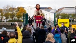 La pequeña Amal, una marioneta de 3,5 metros de una refugiada siria de 10 años, cruza el Puente Millennium, cerca del lugar donde se celebra la cumbre del clima de Naciones Unidas COP26 en Glasgow, Escocia, el 9 de noviembre de 2021. (AP Foto/Alberto Pezzali)