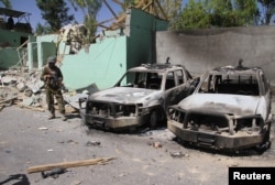 A member of the Afghan security forces stands guard next to damaged army vehicles after a Taliban attack in Ghazni city, Afghanistan, Aug. 15, 2018.