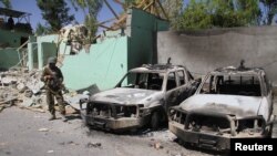 FILE - A member of the Afghan security forces stands guard next to damaged army vehicles after a Taliban attack in Ghazni city, Afghanistan, Aug. 15, 2018.