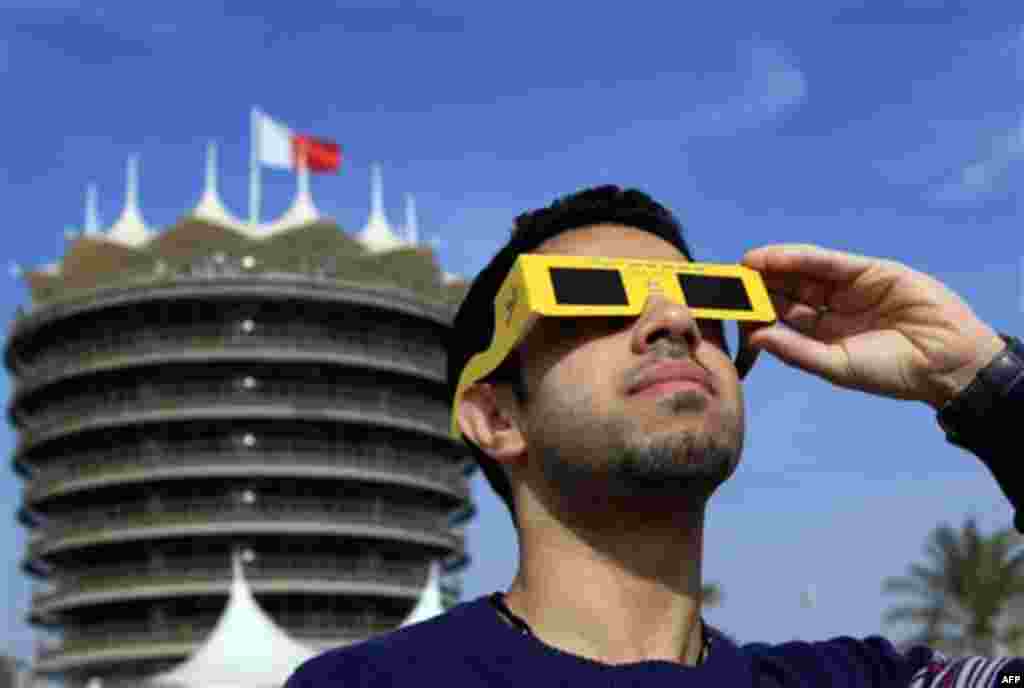 Salman Madhi, a 23-year-old Bahraini, watches a partial solar eclipse Tuesday, Jan. 4, 2011, near the tower of the Bahrain International Circuit, in Sakhir, Bahrain, where the 2011 Formula One car racing season kicks off March 11-13. The partial eclipse w