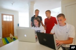 Kel Kelly, back left, and her children Julia McGovern, 18, front left, Shaun McGovern, 16, right, and Patrick McGovern, 14, gather around their computers at their vacation home in Wellfleet, Mass.