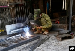 FILE - A man welds an iron door at his workshop in Hanoi, Vietnam.