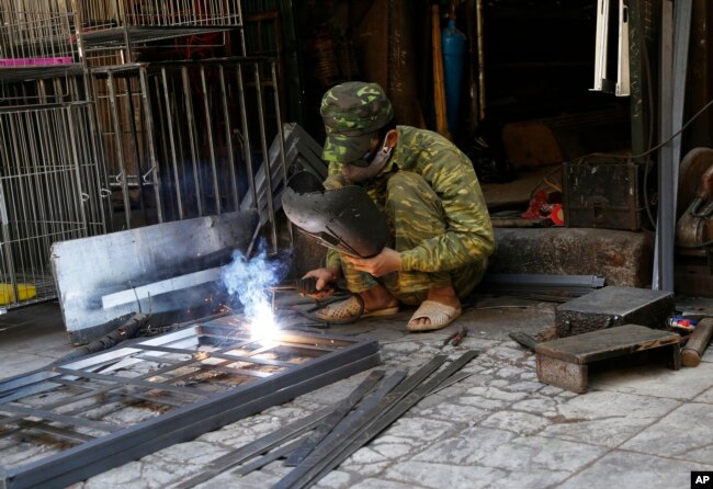 FILE - A man welds an iron door at his workshop in Hanoi, Vietnam.