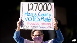 Demonstrator Gina Dusterhoft holds up a sign as she walks to join others standing across the street from the federal courthouse in Houston, Texas, Nov. 2, 2020, before a hearing involving drive-thru ballots cast in Harris County.