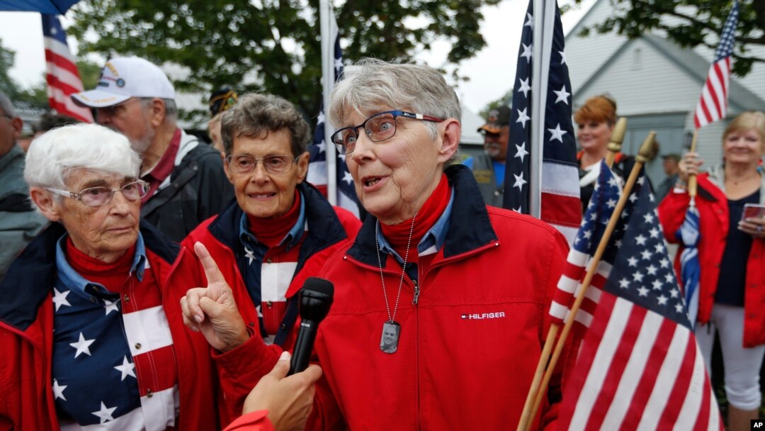 FILE - The Freeport Flag Ladies, Carmen Footer, from left, JoAnn Miller and Elaine Greene, wave to vehicles in Freeport, Maine, Aug. 23, 2011.