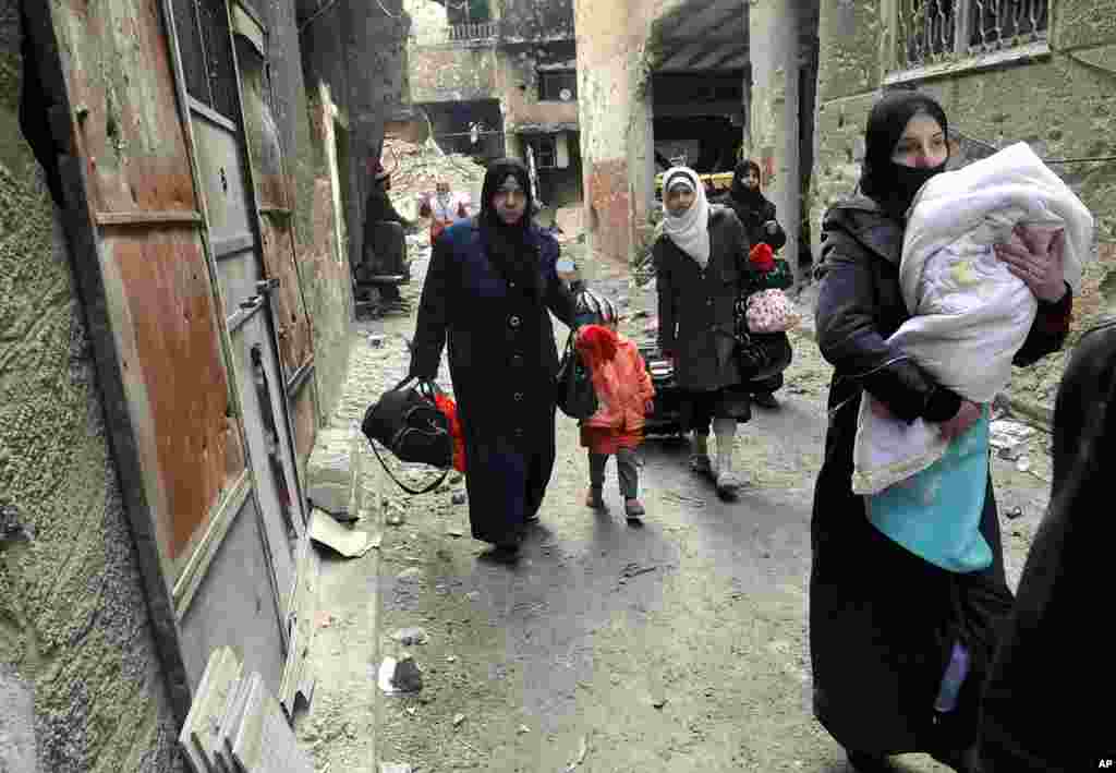 This photo released by the Syrian official news agency SANA shows residents of the besieged Yarmouk Palestinian refugee camp carrying their belongings as they flee the camp on the southern edge of Damascus, Feb. 4, 2014. 