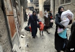 FILE - This photo released by the Syrian official news agency SANA shows residents of the besieged Yarmouk Palestinian refugee camp carry their belongings as they flee the camp on the southern edge of Damascus, Feb. 4, 2014.