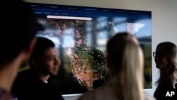 Employees of German startup OroraTech stand in front of a screen showing wildfires in Canada and the United States via satellites in Munich, Germany, Sept. 13, 2023. The Munich-based company analyzes satellite images with artificial intelligence.