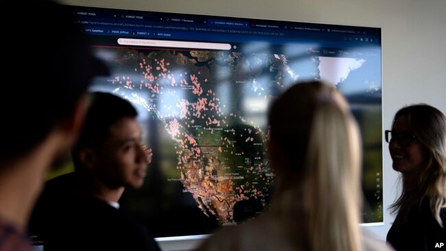 Employees of German startup OroraTech stand in front of a screen showing wildfires in Canada and the United States via satellites in Munich, Germany, Sept. 13, 2023. The Munich-based company analyzes satellite images with artificial intelligence.