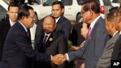 Prime Minister Hun Sen, left, shakes hands with Deputy Prime Minister Minister of the Interior Sar Kheng as they arrive to attend a ceremony for the 68th anniversary of the founding of the Cambodian People's Party, in Phnom Penh, Cambodia, Friday, June 28, 2019. (AP Photo)