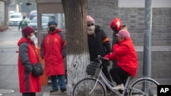Neighborhood watch volunteers wear face masks as they gather on a street corner in Beijing, Monday, Jan. 27, 2020. (AP Photo/Mark Schiefelbein)